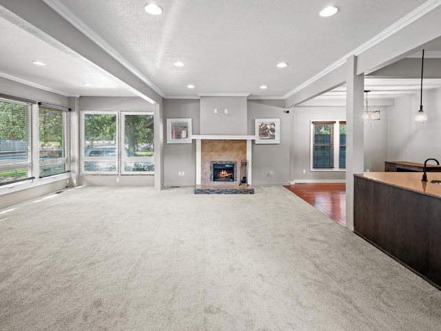 unfurnished living room with a warm lit fireplace, a textured ceiling, carpet flooring, and crown molding