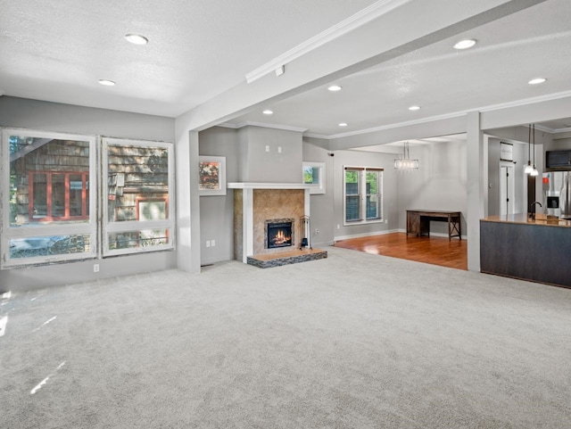 unfurnished living room featuring a warm lit fireplace, a textured ceiling, carpet, and crown molding