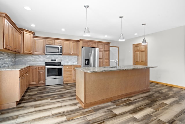 kitchen with light stone countertops, an island with sink, stainless steel appliances, and sink