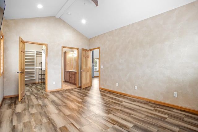 unfurnished bedroom featuring beamed ceiling, a closet, wood-type flooring, a spacious closet, and connected bathroom