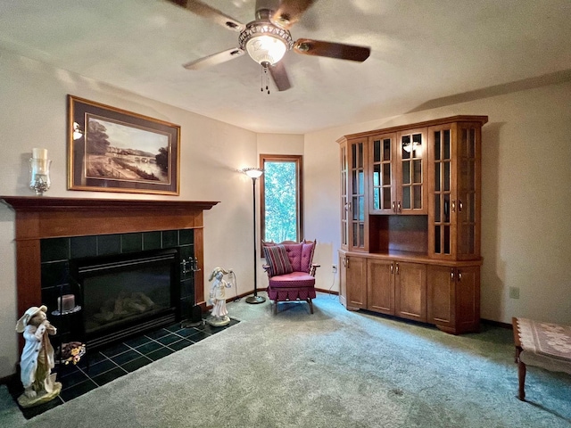 sitting room with a tiled fireplace, dark carpet, and ceiling fan