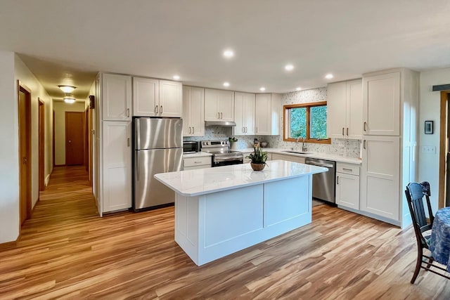 kitchen featuring under cabinet range hood, stainless steel appliances, light wood-style floors, and a sink