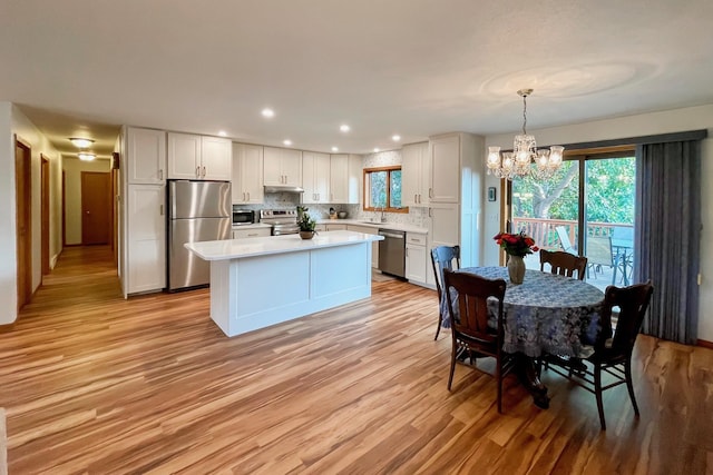 kitchen with a kitchen island, stainless steel appliances, decorative backsplash, light countertops, and light wood-type flooring