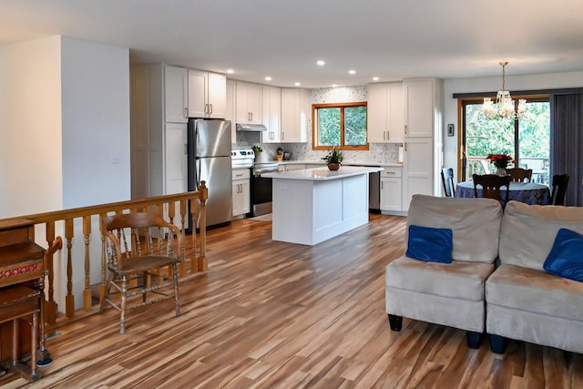 kitchen featuring under cabinet range hood, tasteful backsplash, open floor plan, stainless steel appliances, and light countertops