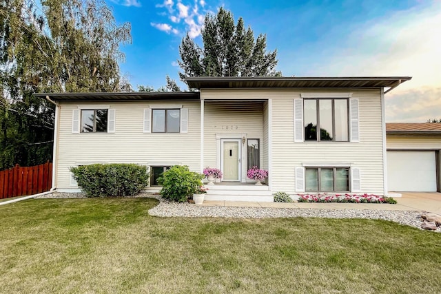 bi-level home featuring an attached garage, concrete driveway, a front yard, and fence