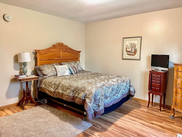 bedroom with wood finished floors, baseboards, and a textured ceiling