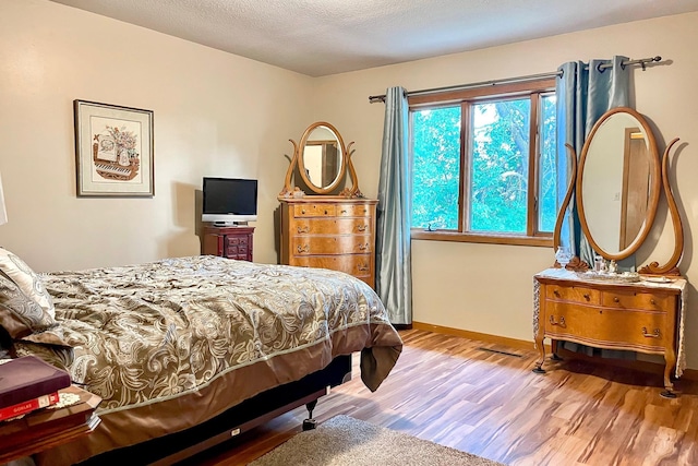 bedroom featuring a textured ceiling, baseboards, and wood finished floors