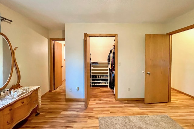 bedroom with a spacious closet, light wood-style floors, a closet, and baseboards