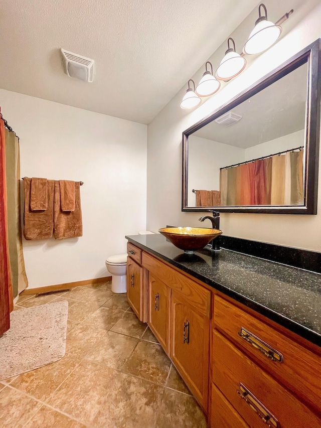 full bath featuring vanity, baseboards, visible vents, a textured ceiling, and toilet