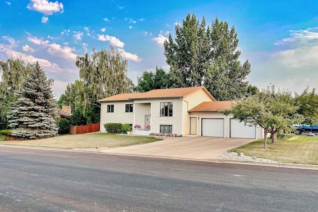 split foyer home featuring concrete driveway, fence, a garage, and a front lawn