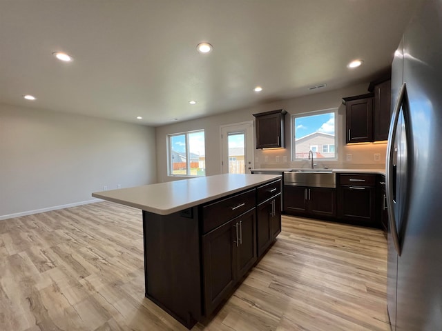 kitchen featuring light wood-type flooring, stainless steel refrigerator, a center island, sink, and dark brown cabinetry