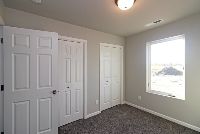 unfurnished bedroom with dark carpet and two closets