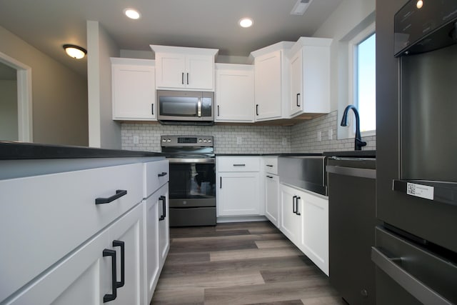 kitchen with dark wood-type flooring, appliances with stainless steel finishes, backsplash, and white cabinetry