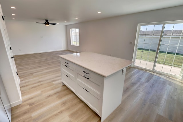 kitchen featuring a center island, light wood-type flooring, light stone countertops, white cabinetry, and ceiling fan