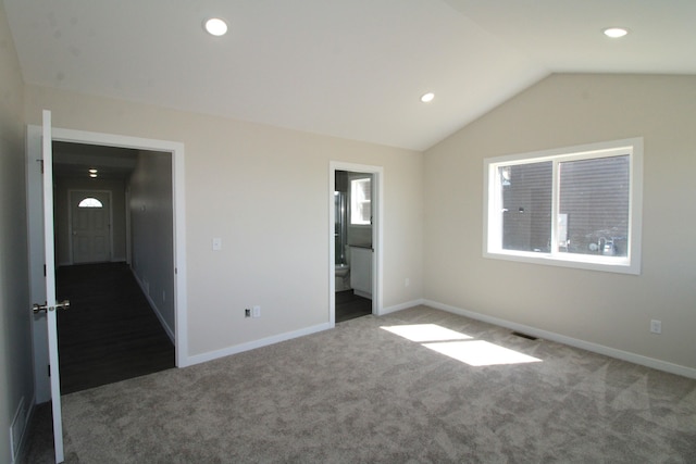 unfurnished bedroom featuring dark carpet, vaulted ceiling, and ensuite bath