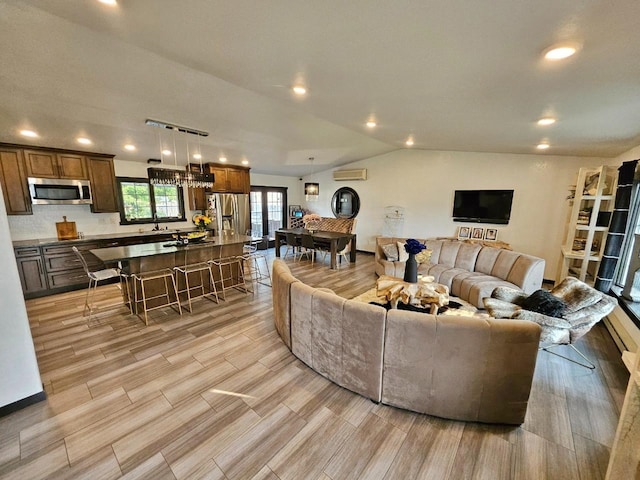 living room with lofted ceiling, light hardwood / wood-style floors, an AC wall unit, and sink