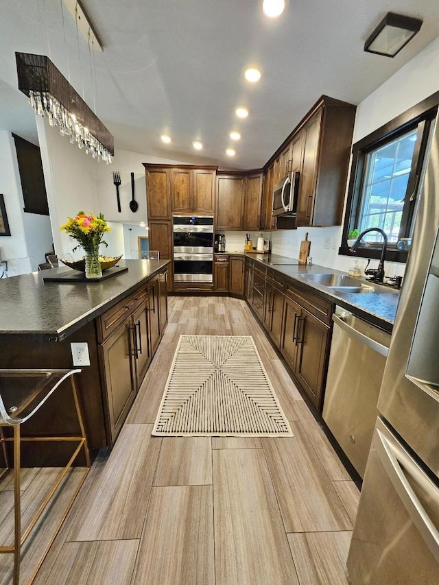 kitchen with light hardwood / wood-style flooring, stainless steel appliances, sink, dark brown cabinets, and pendant lighting