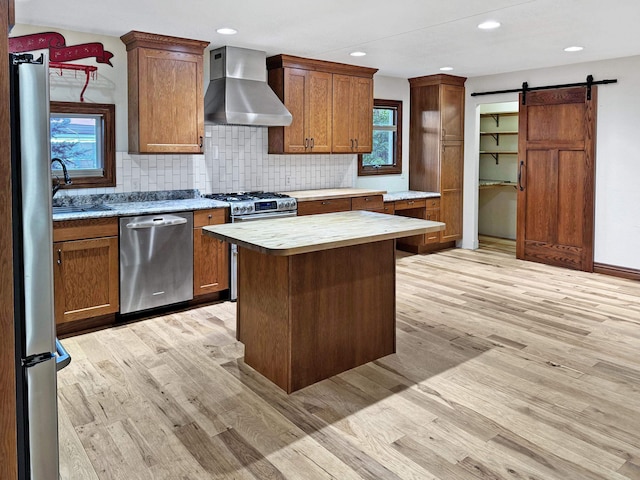 kitchen featuring a kitchen island, a barn door, wall chimney exhaust hood, light hardwood / wood-style flooring, and appliances with stainless steel finishes