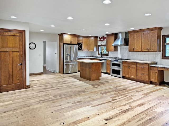 kitchen with light hardwood / wood-style floors, a kitchen island, stainless steel appliances, sink, and wall chimney range hood