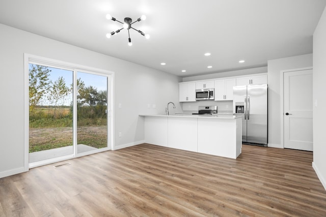 kitchen featuring light hardwood / wood-style flooring, appliances with stainless steel finishes, kitchen peninsula, and white cabinetry