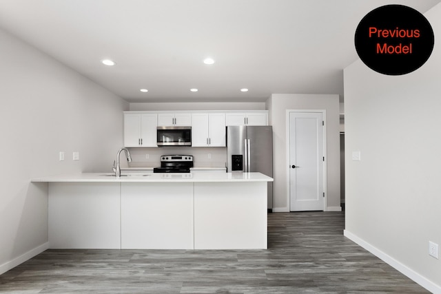 kitchen with appliances with stainless steel finishes, white cabinetry, kitchen peninsula, dark hardwood / wood-style flooring, and sink