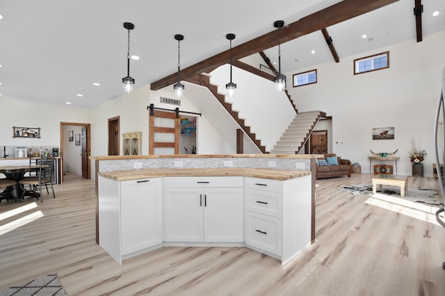 kitchen with beam ceiling, white cabinetry, hanging light fixtures, a barn door, and light hardwood / wood-style flooring