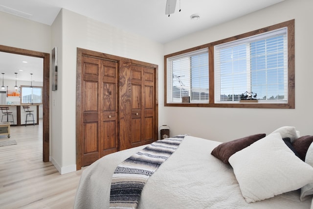 bedroom with multiple windows, light wood-type flooring, ceiling fan, and a closet