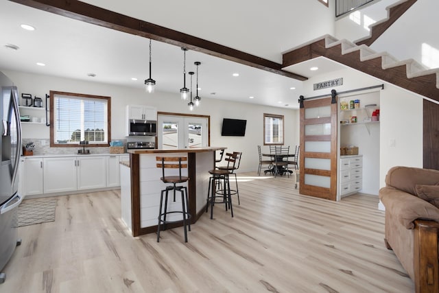 kitchen with hanging light fixtures, light hardwood / wood-style floors, white cabinetry, a barn door, and stainless steel appliances