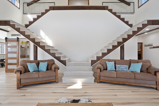 unfurnished living room featuring light hardwood / wood-style floors, a barn door, and a high ceiling