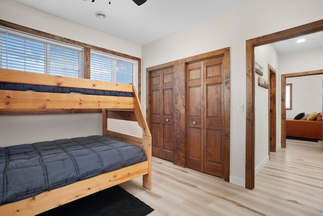 bedroom with light wood-type flooring, multiple closets, and ceiling fan