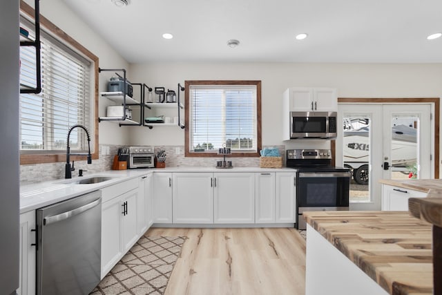 kitchen with light wood-type flooring, tasteful backsplash, sink, white cabinetry, and stainless steel appliances