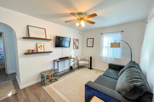 living area featuring a ceiling fan, wood finished floors, arched walkways, and baseboards