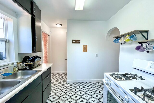 kitchen with light floors, baseboards, white range with gas cooktop, a sink, and light countertops