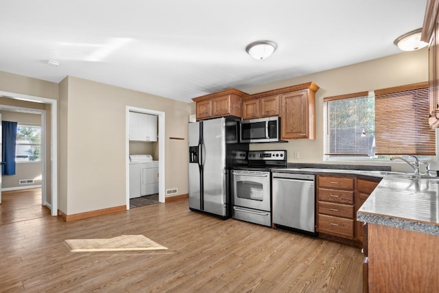 kitchen featuring stainless steel appliances, washer and dryer, sink, and light wood-type flooring