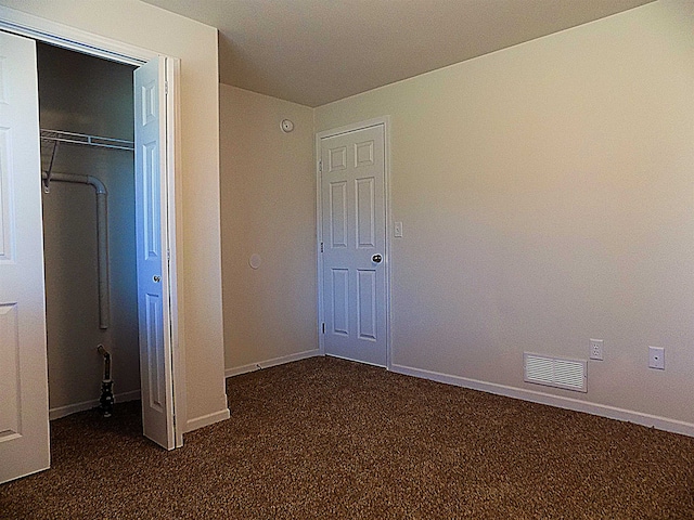 unfurnished bedroom with dark carpet and a closet