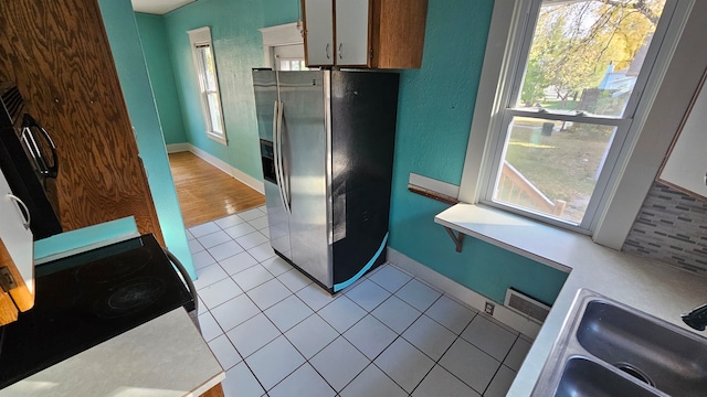 kitchen featuring sink, light tile patterned floors, stove, and stainless steel refrigerator with ice dispenser