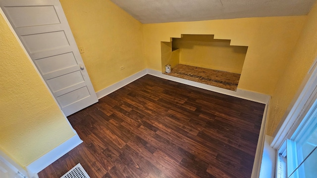 empty room featuring a textured ceiling, vaulted ceiling, and dark hardwood / wood-style flooring