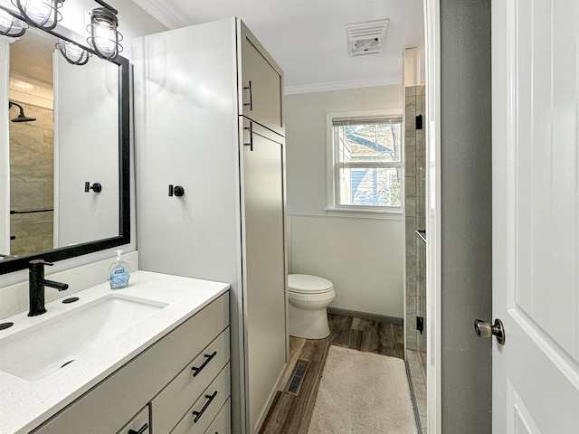 bathroom featuring a shower with shower door, hardwood / wood-style floors, toilet, vanity, and crown molding