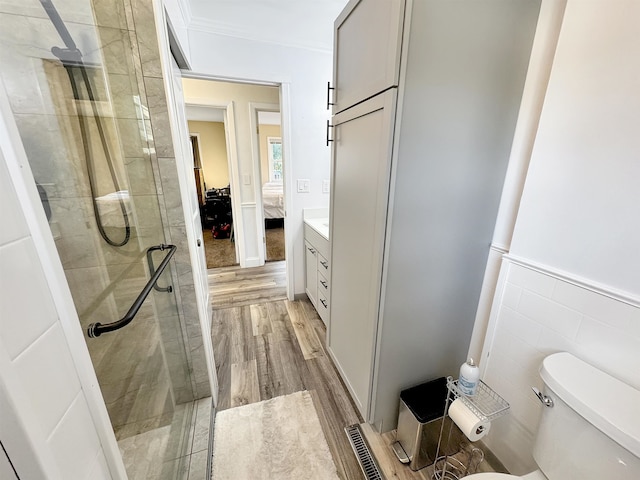 bathroom featuring a shower with door, toilet, hardwood / wood-style floors, tile walls, and vanity