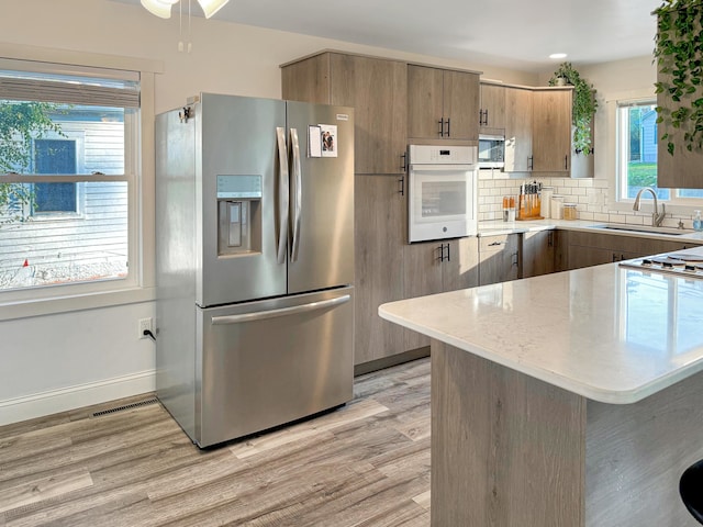 kitchen featuring kitchen peninsula, stainless steel appliances, sink, and light wood-type flooring