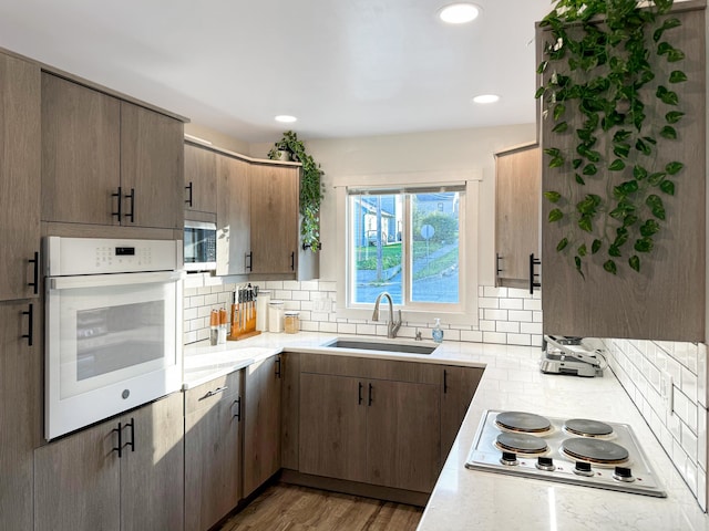 kitchen with backsplash, sink, light wood-type flooring, and white appliances