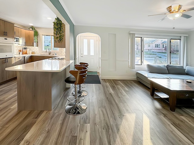 kitchen featuring white oven, backsplash, kitchen peninsula, a kitchen breakfast bar, and light hardwood / wood-style flooring