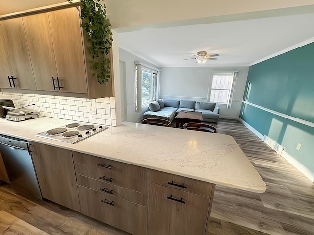 kitchen featuring kitchen peninsula, a wealth of natural light, white stovetop, stainless steel dishwasher, and hardwood / wood-style flooring