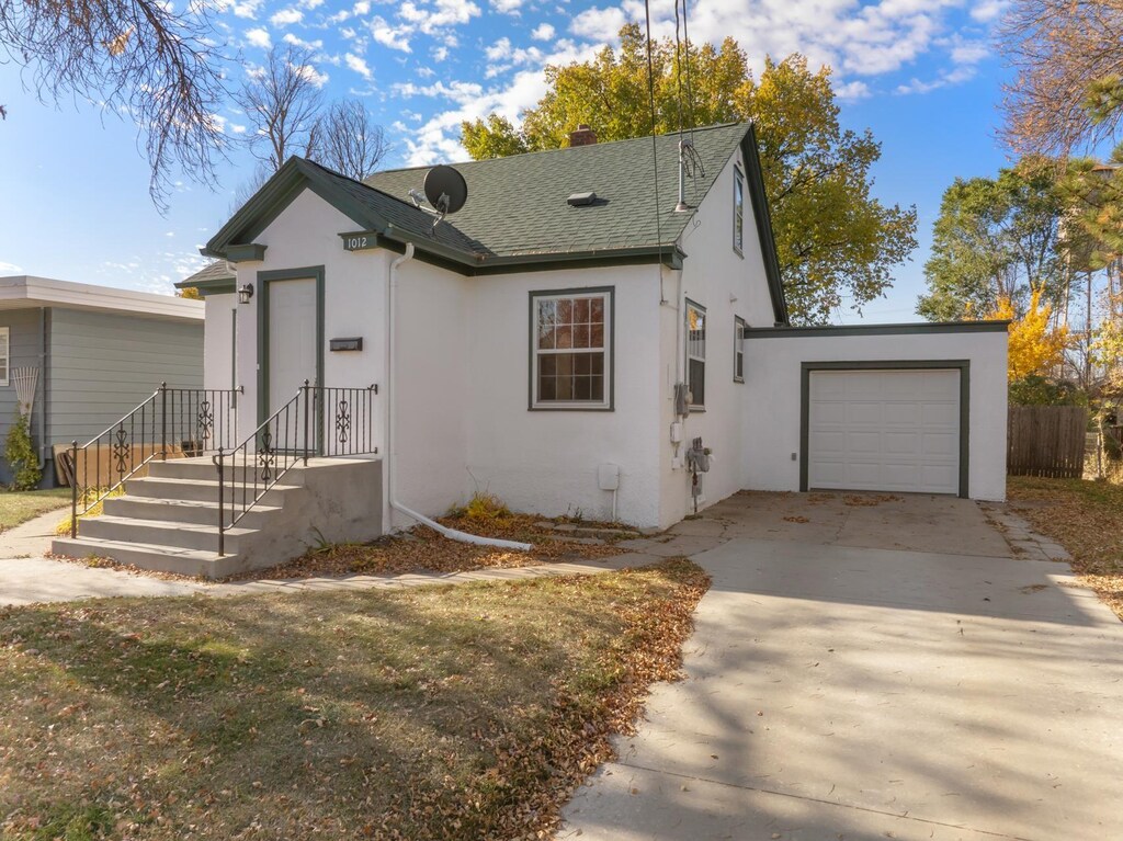 1012 4th St, Minot, ND 58701 - bungalow-style home featuring an attached garage, a shingled roof, stucco siding, and concrete driveway