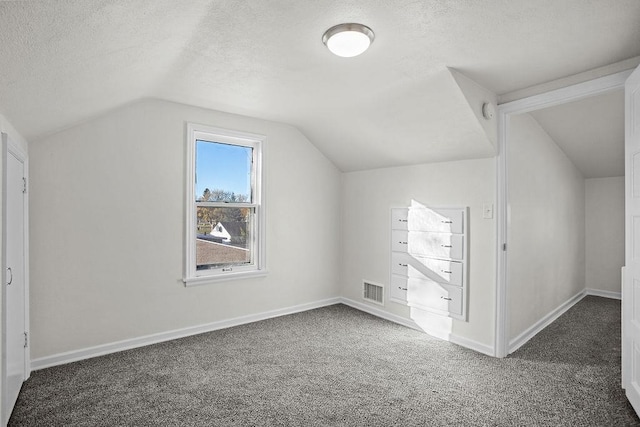 additional living space with a textured ceiling, vaulted ceiling, and dark colored carpet