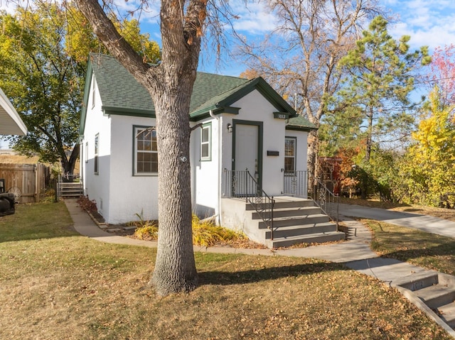 1012 4th St, Minot, ND 58701 - bungalow featuring fence, a shingled roof, stucco siding, and a front lawn