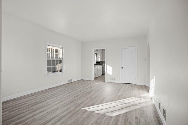 1012 4th St, Minot, ND 58701 - unfurnished room featuring arched walkways, baseboards, light wood-style flooring, and visible vents