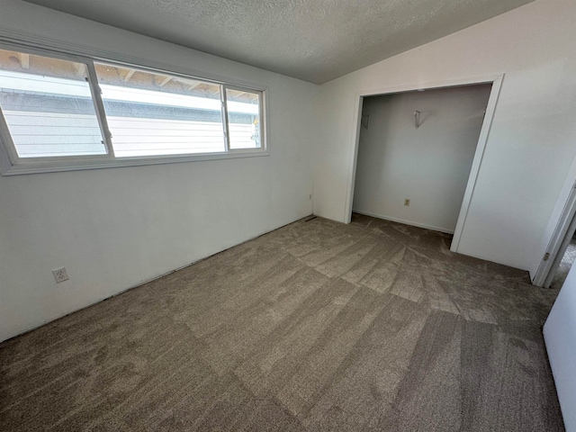 unfurnished bedroom with dark carpet, vaulted ceiling, a textured ceiling, and a closet