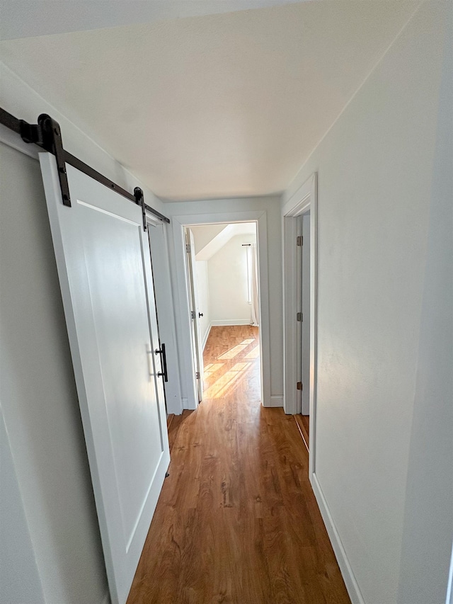 hallway featuring wood finished floors, baseboards, and a barn door