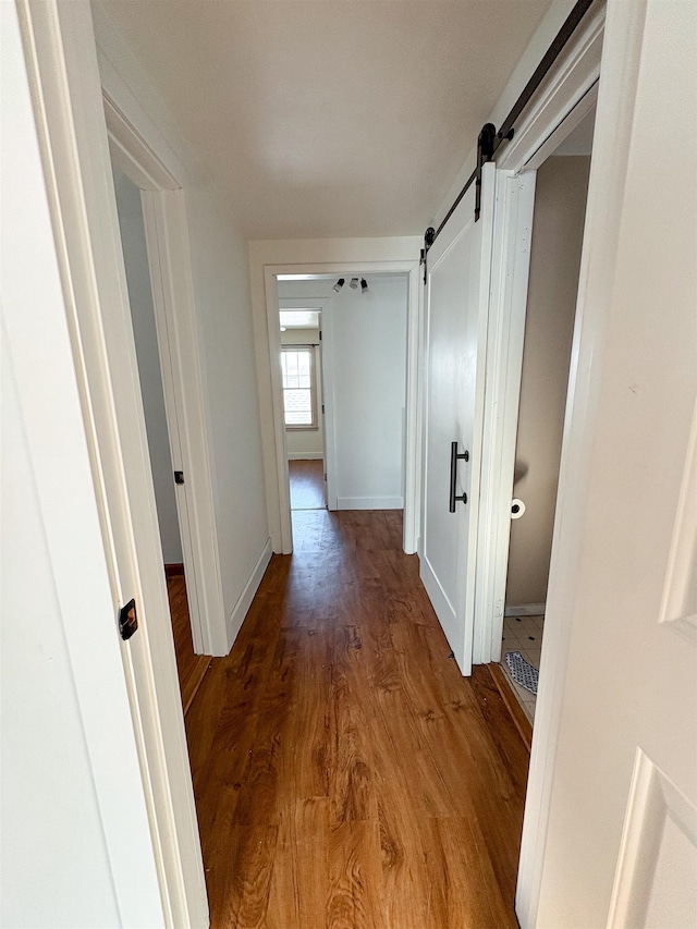 hall featuring a barn door, baseboards, and wood finished floors